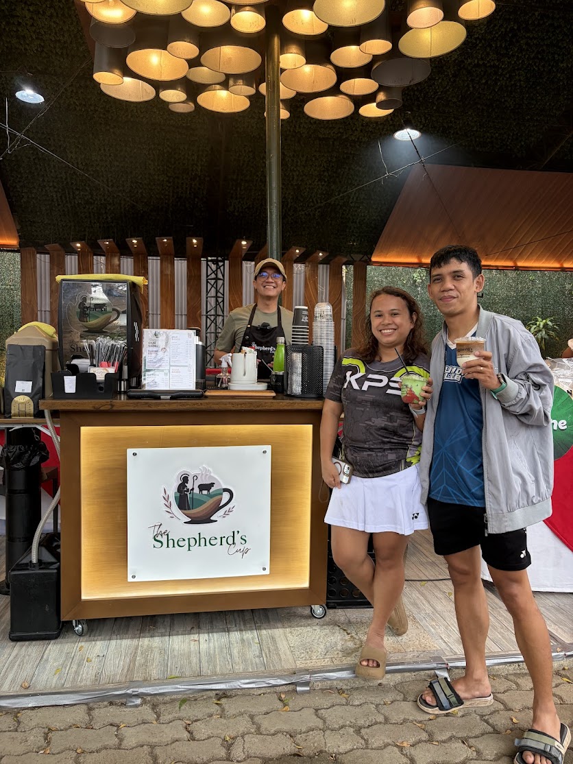 The Shepherd's Cup cart with illuminated brand signage, barista at the bar, and two customers smiling with drinks